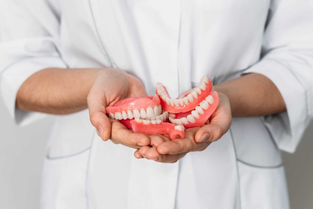 Prosthetist holding dentures in their hand | Featured image for How Long Do Dentures Last? Blog on Pearl Denture Studio.