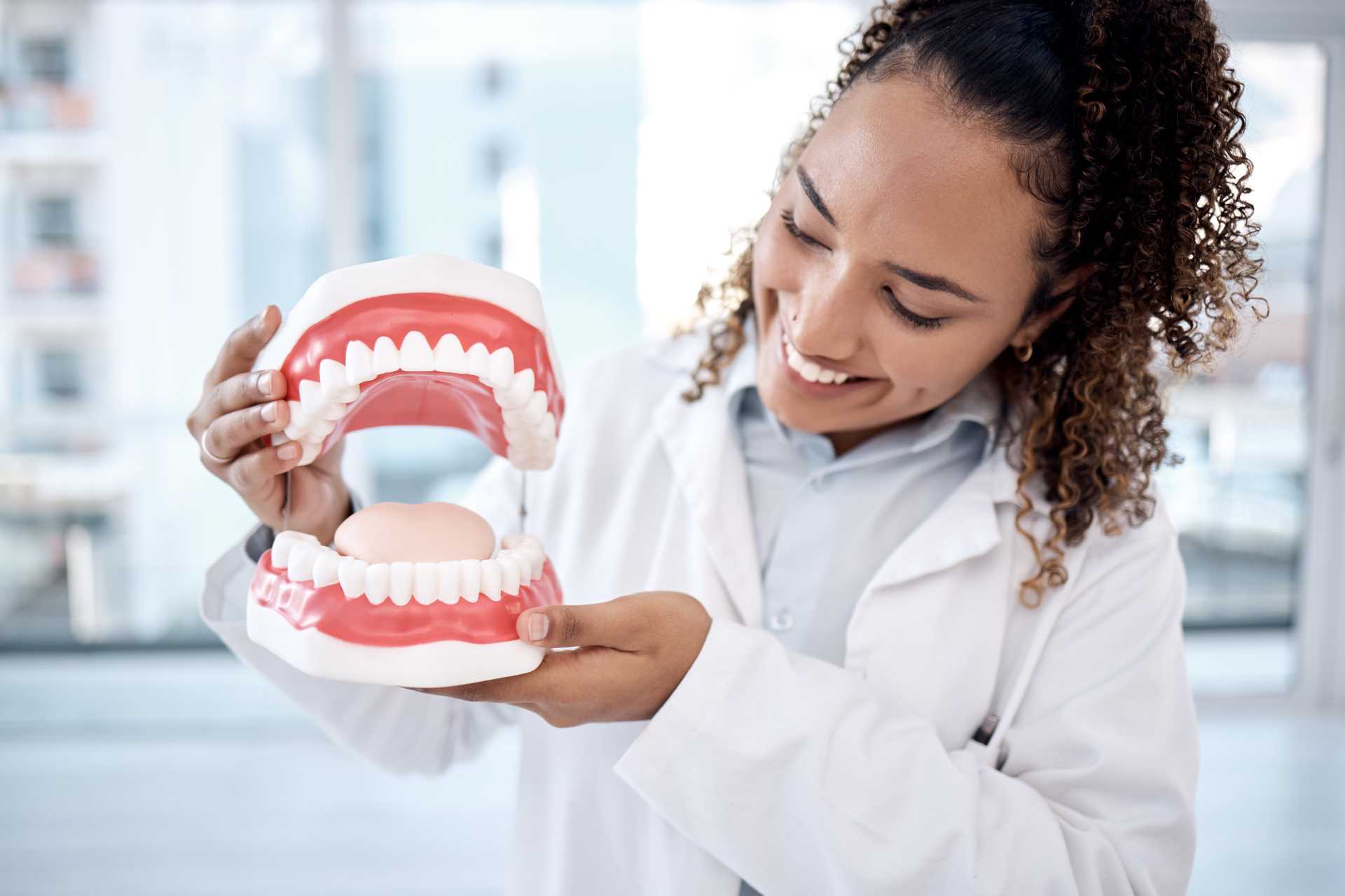 Dentist holding a large model of teeth | Featured image for the Impact of Oral Health on General Health blog by Pearl Denture Studio.