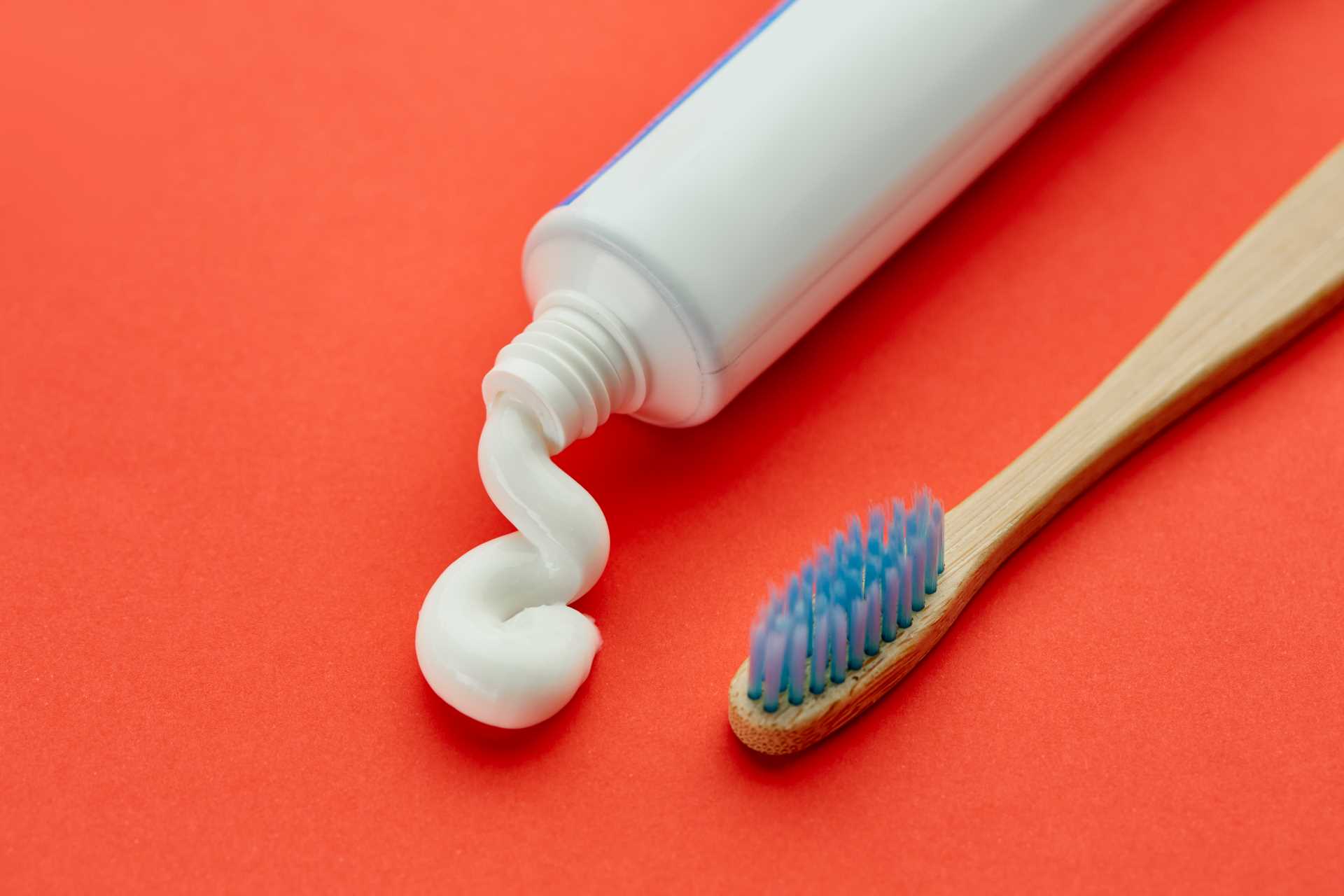 Toothpaste and toothbrush set down on a red table | Featured image for the Toothpaste Ingredients: The Good & The Bad blog by Pearl Denture Studio.